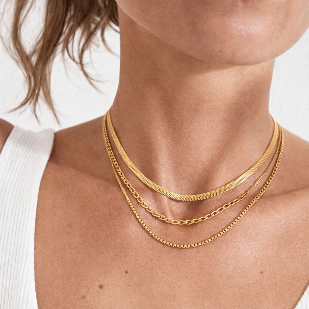 Layered 3-in-1 gold necklace with herringbone, figaro, and box chains worn on model neck